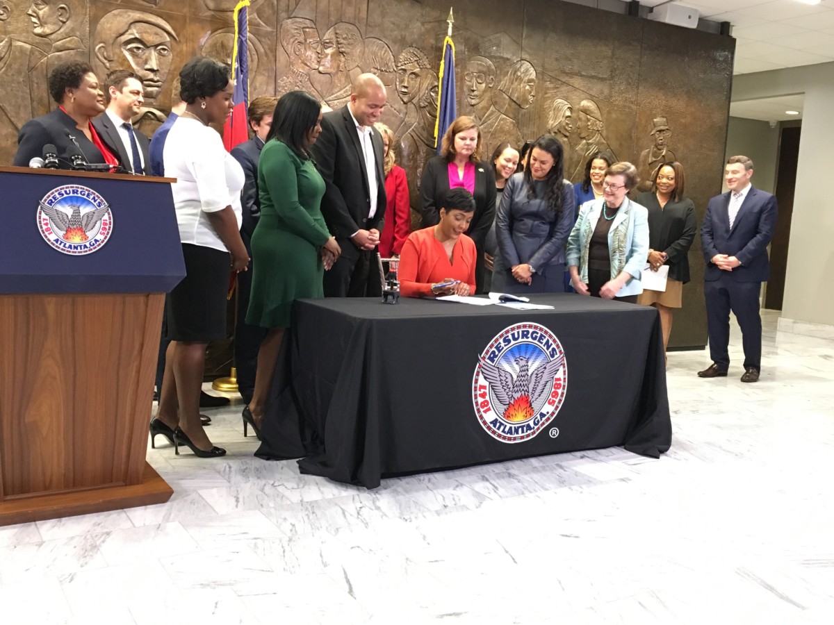 Atlanta Mayor Keisha Lance Bottoms signs an ordinance Tuesday to start transferring dozens of disputed property deeds to the city school system. School Superintendent Maria Carstarphen stands to Bottoms' left and other officials from the city and schools look on. Credit: Maggie Lee
