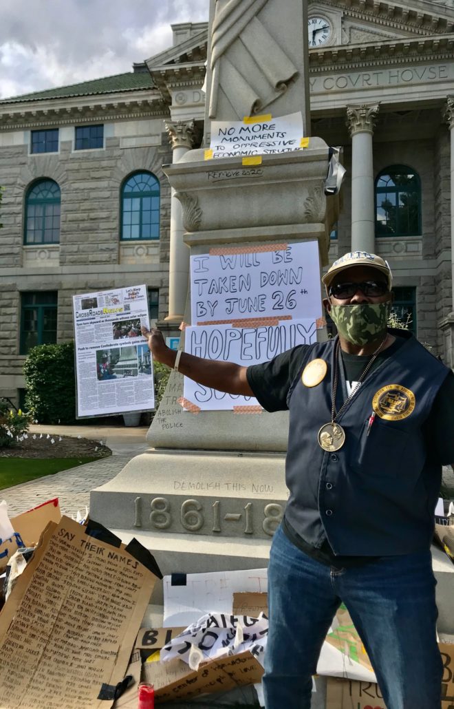 A man in front of the obelisk, which is covered in signs.